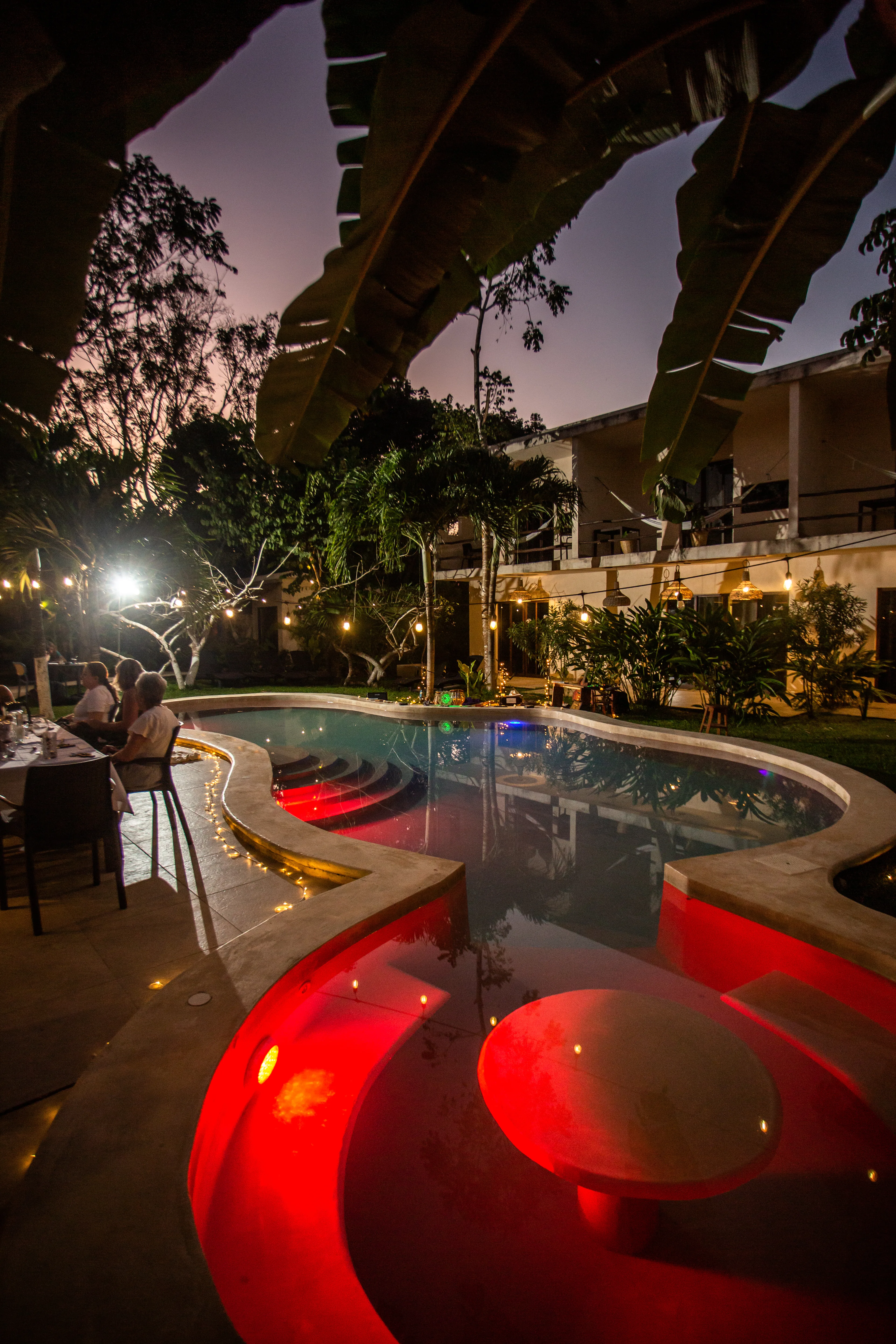 Pool at dusk with red underwater lighting and a dinner table